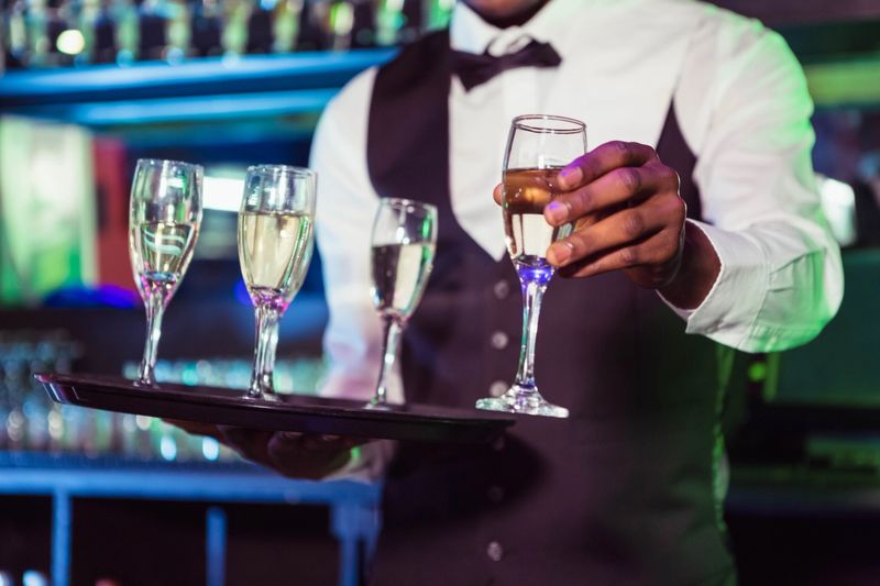 Bartender holding a tray of glasses and serving champagne in bar