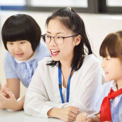 Teacher engaging with two young students at a table.