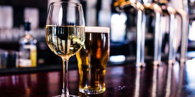 A glass of white wine and a pint of beer on a bar counter.