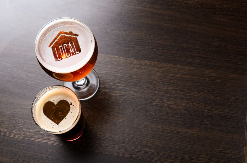 Loving local craft beer. House and heart silhouettes in two glasses of fresh beer on pub table, view from above