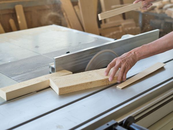 Hand guiding wood through a table saw blade in a workshop.