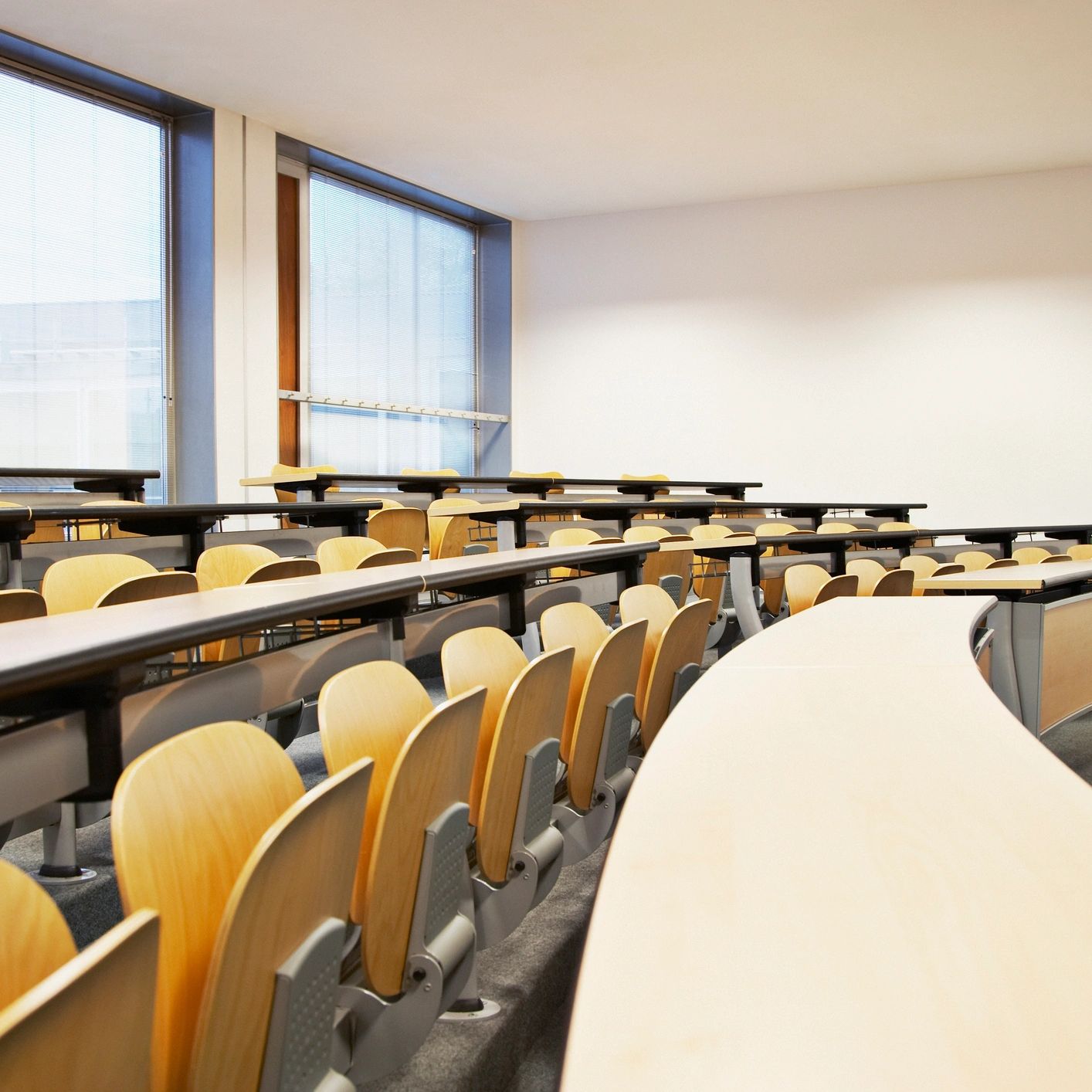 Empty modern lecture hall with wooden seats and large windows.