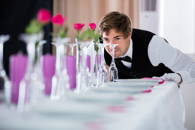 Handsome Waiter Looking At Wedding Table Arrangement At Restaurant