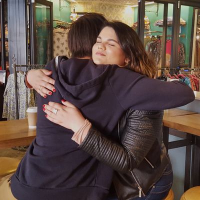 Two women sharing a warm hug in a cozy, colorful shop.