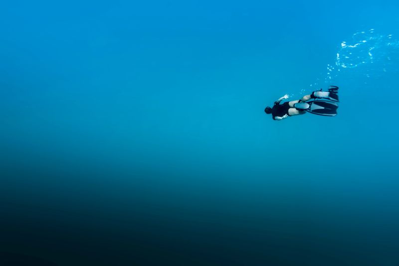 A DSLR Canon underwater photo of a 41-year-old Brazilian man free diving into clear turquoise water at Baía do Sancho in Fernando de Noronha, Pernambuco, Brazil.
