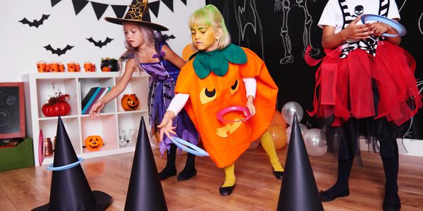 Kids in Halloween costumes playing ring toss with witch hats indoors.