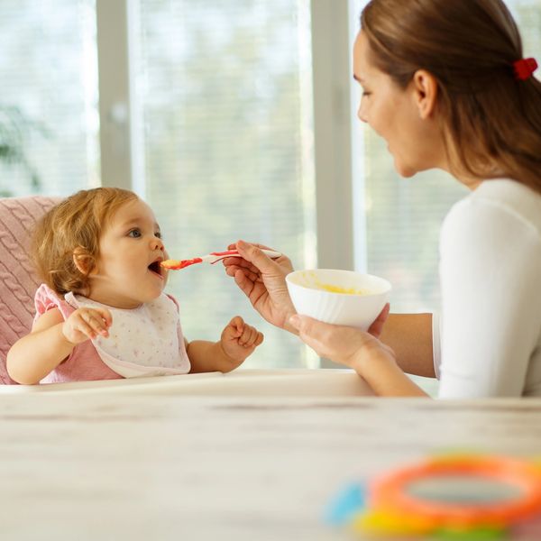 Mother feeding her baby with a spoon at the table.