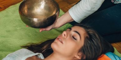 A woman lying down receiving a sound therapy session with a Tibetan singing bowl.
