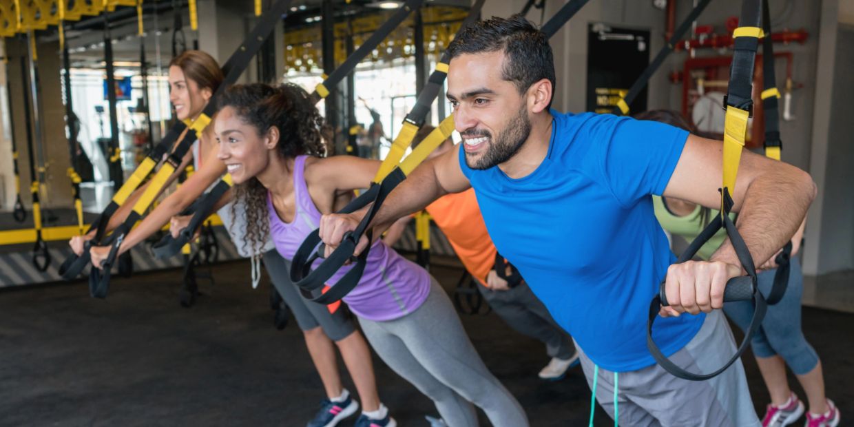Personas hacen ejercicio con correas de suspensión en un gimnasio.