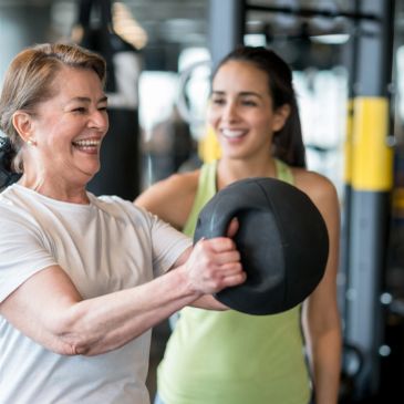 Senior woman exercising with a kettlebell, guided by a trainer.