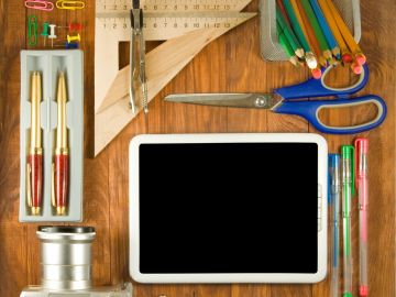 Workspace with tablet and stationery on wooden table.