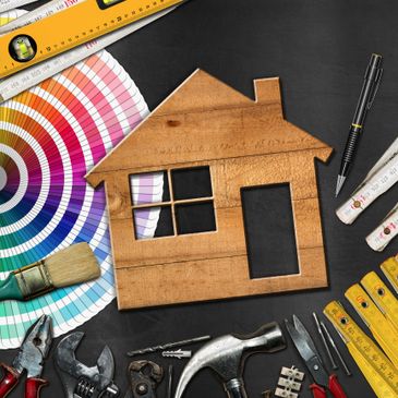 Wooden house model surrounded by tools and color swatches on a black surface.