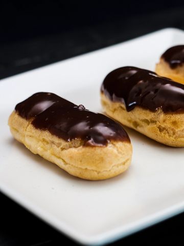 Three chocolate-glazed éclairs on a white plate.
