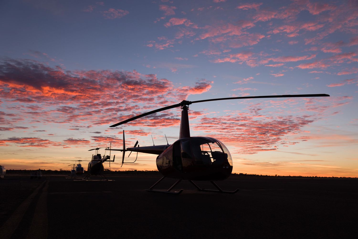 Helicopters lined up on a runway at sunset with pink clouds.