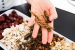 Hand holding dried herbs and spices over bowls of various dried ingredients.