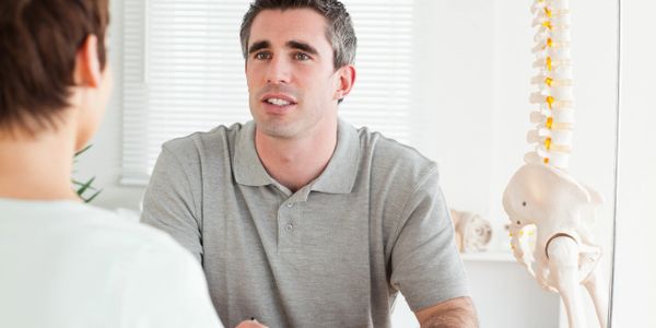 A doctor consulting with a patient near a spine model in a medical office.