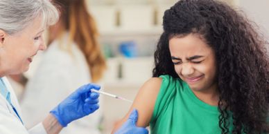 Young girl receiving a vaccine shot with a tense expression from a smiling healthcare worker.