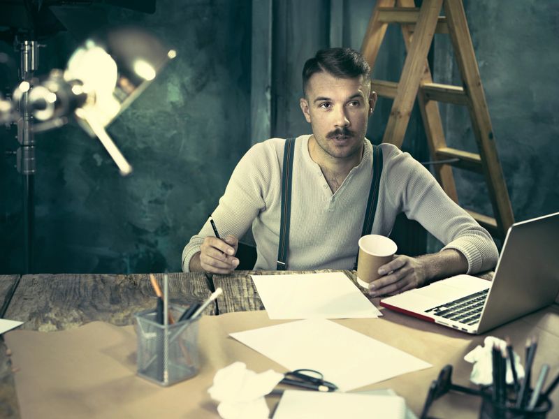 Portrait of a bearded businessman who is working with his notebook at loft studio or home.