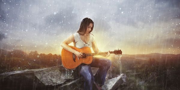 Woman playing guitar outdoors in the rain at sunset.