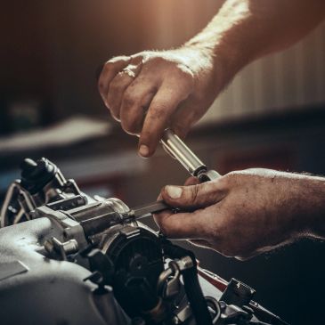 Hands repairing a mechanical part with a tool.
