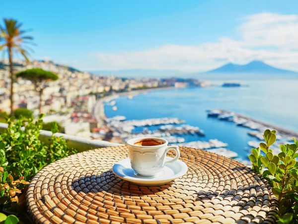 A cup of coffee on a table overlooking a sunny coastal city and marina.