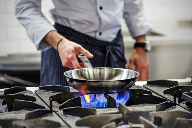 Frying pan on a gas stove. Chef controls the cooking process