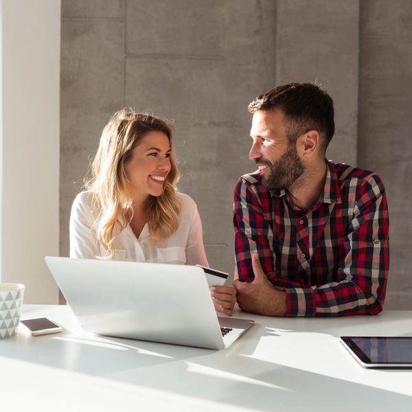 Happy couple using a laptop and credit card at a bright workspace.