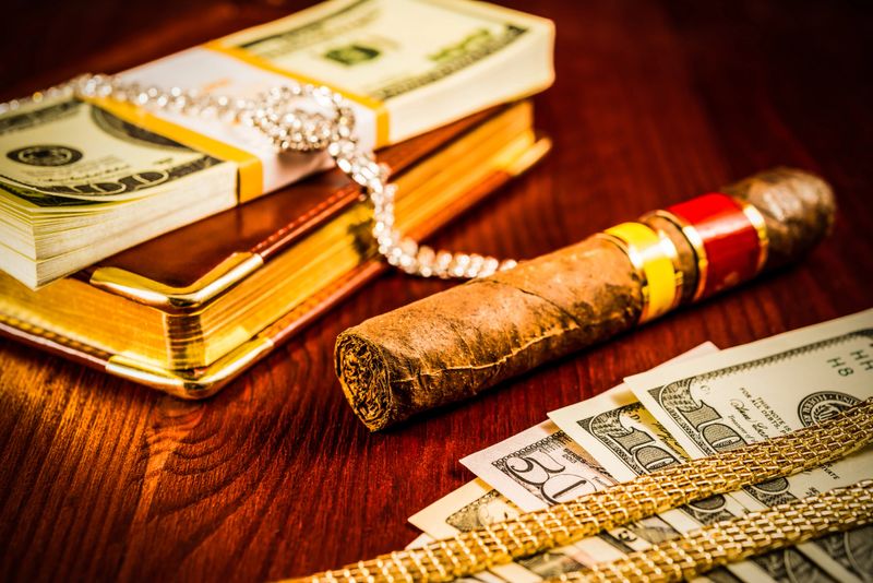 Money with a leather diary and cuban cigar with jewellery on a mahogany table