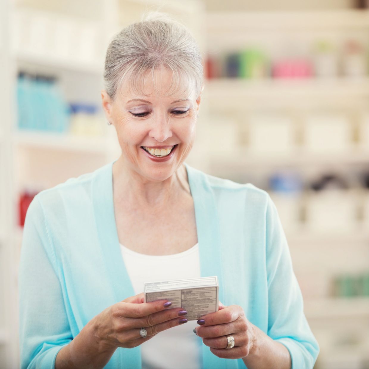 Smiling mature woman reading product information on a box in a store.