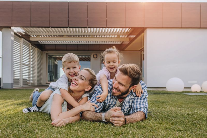 Happy parents having fun with their children while lying on grass in the front yard.