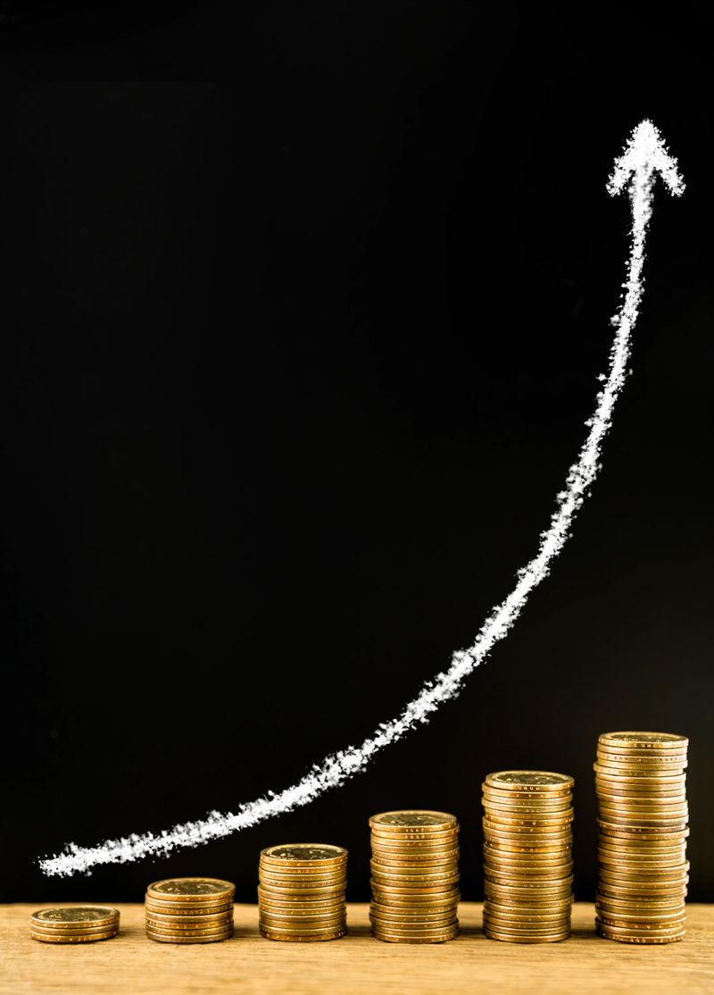 Money coin stack arranged as a graph on a wooden and draw arrow with white chalk on blackboard, concept of money growth