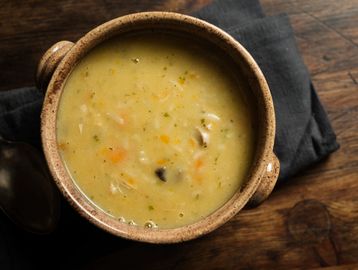 A bowl of creamy chicken and vegetable soup on a wooden table.