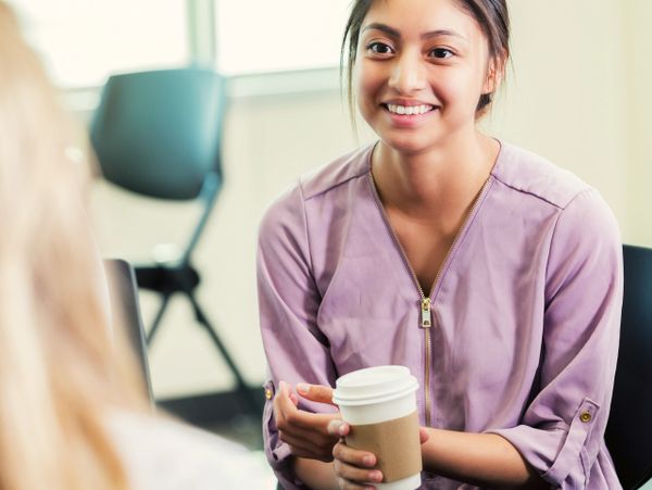 Smiling woman in casual attire holding a coffee cup during a conversation.