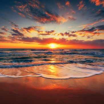 Sunset over ocean waves gently washing onto the sandy shore.