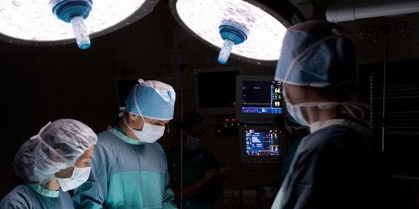 Surgeons in blue scrubs perform surgery under bright operating room lights.