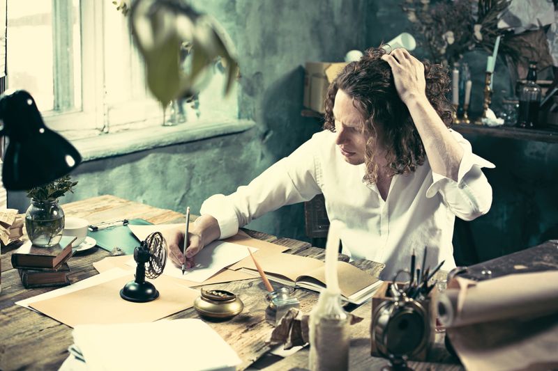 Writer at work. Handsome young writer sitting at the table and writing something in his sketchpad at home