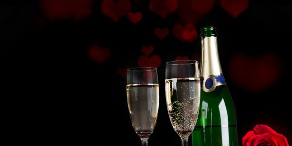 Romantic champagne setup with roses and heart bokeh on black background.