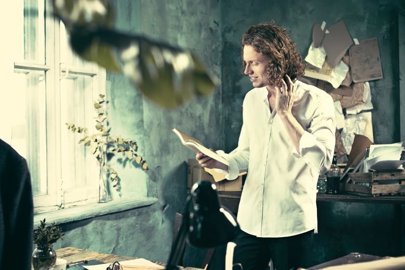 Writer at work. Handsome young writer standing near the table and making up something in his mind at home