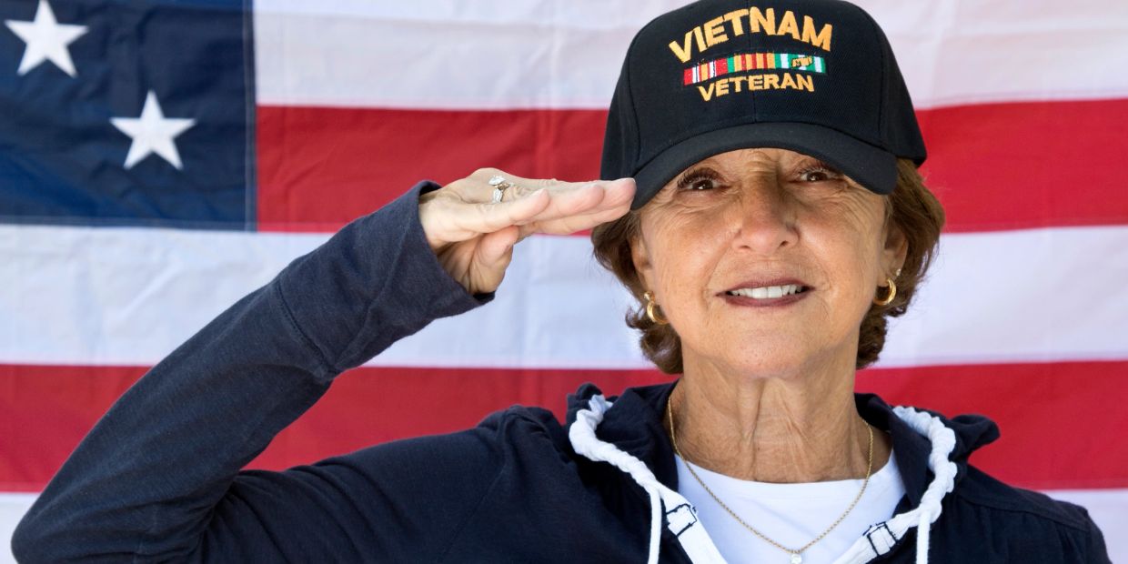Woman saluting with a Vietnam veteran hat in front of American flag.