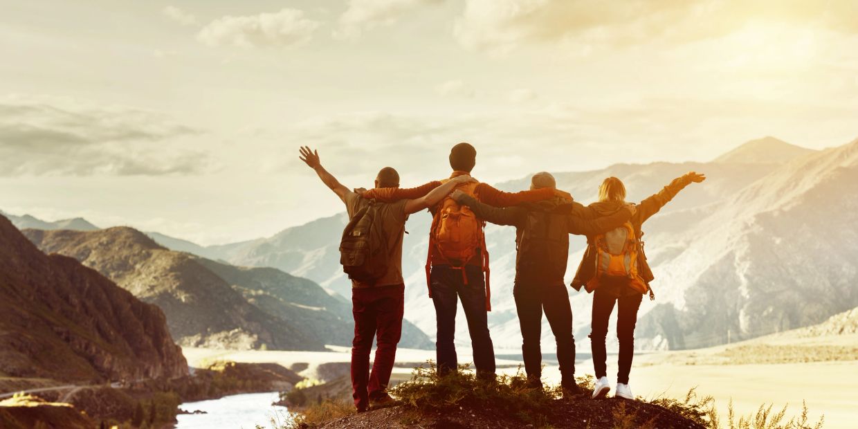 Four friends hiking in the mountains with arms around each other.