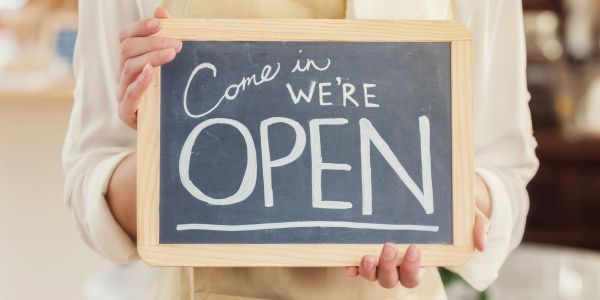 A person holding a chalkboard sign that says "Come in, we're OPEN."