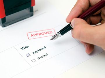 Person marking approved on visa application with stamp nearby.