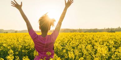 Lady holding her arms up in the air in a  field of yellow flowers