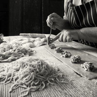 Hands preparing homemade pasta with meat filling on a wooden table.