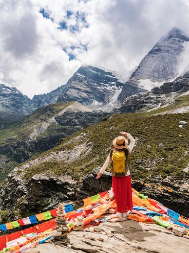 A woman stands on a mountain, looking at a larger mountain.