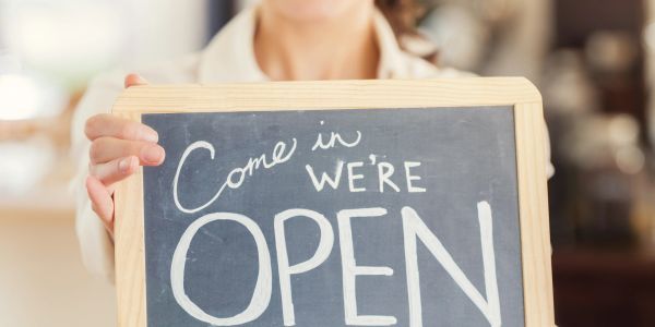 Person holding a sign that says "Come in, we're OPEN".