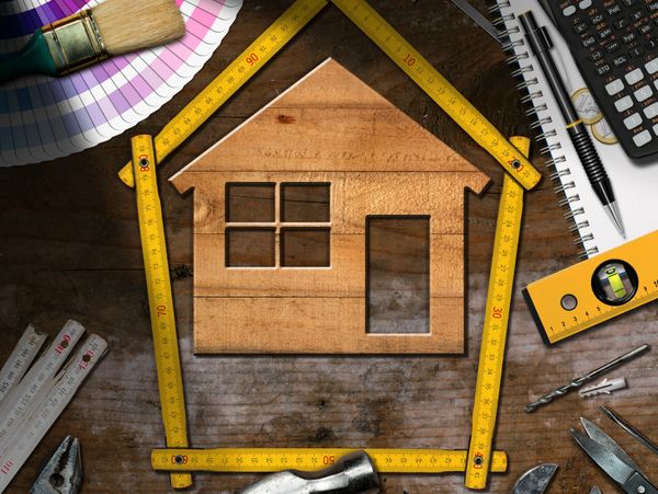 House outline made with measuring tape surrounded by construction tools on wood.