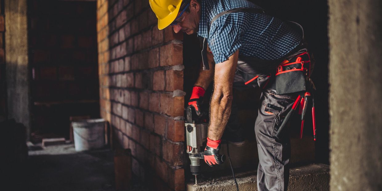 Construction worker using a drill on a concrete base inside a building.