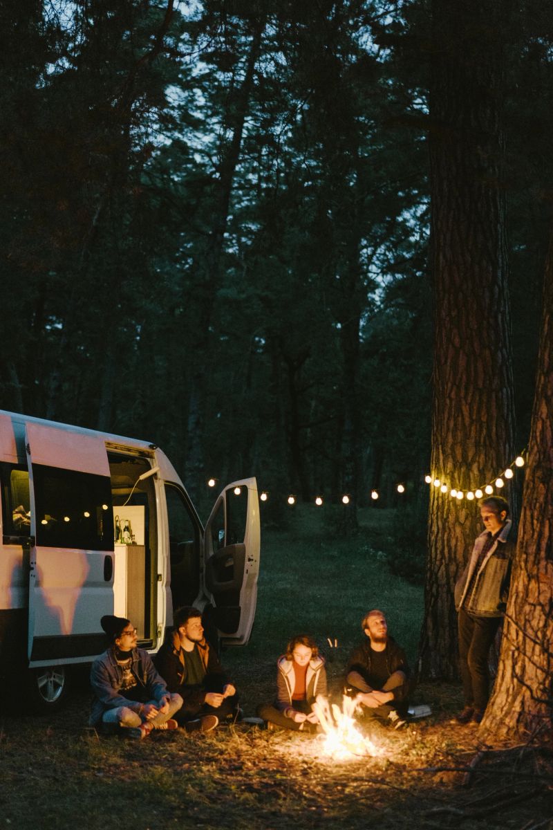 Young Caucasian men and woman  sitting near campfire in the forest near the camper van