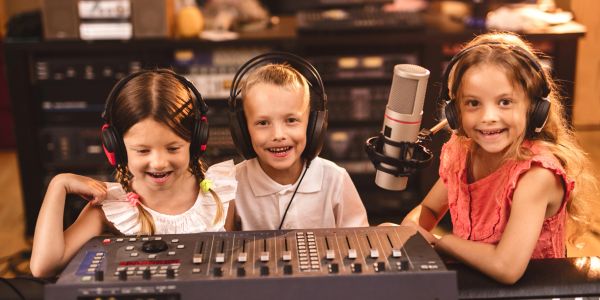 Three children in a recording studio with headphones and a microphone.